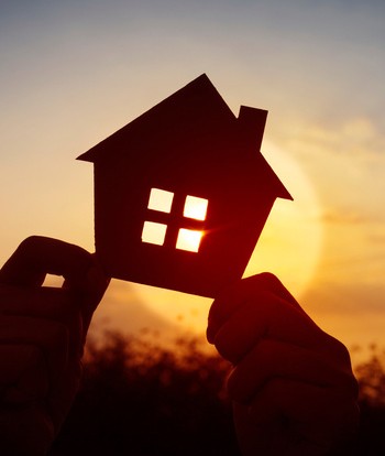 ombre de deux mains qui tiennent une petite maison, devant le soleil couchant
